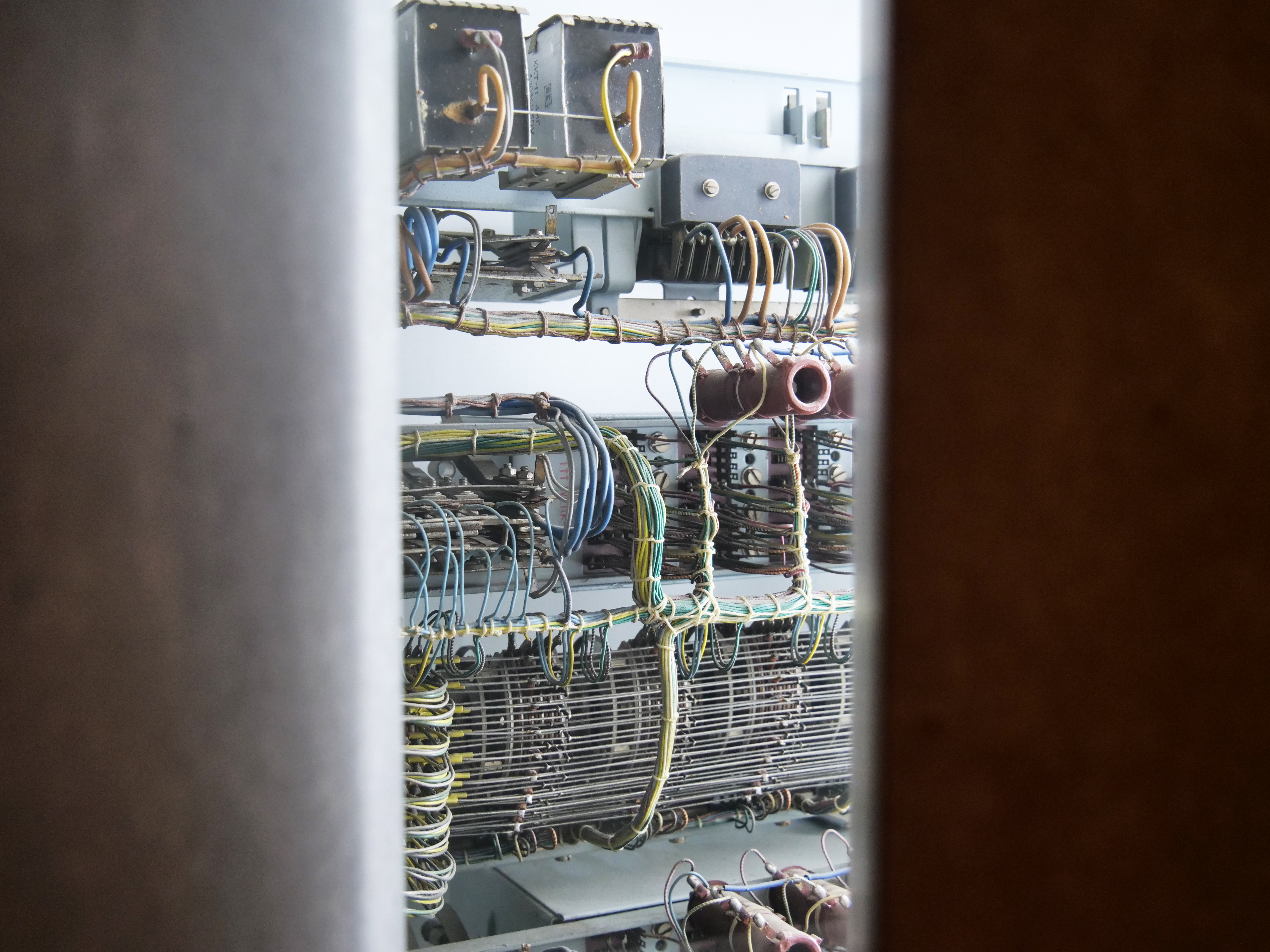 AI generated: The image shows the internal wiring of an old electrical or electronic device with rows of wires and components. These are enclosed in a housing or room and appear through a narrow gap.