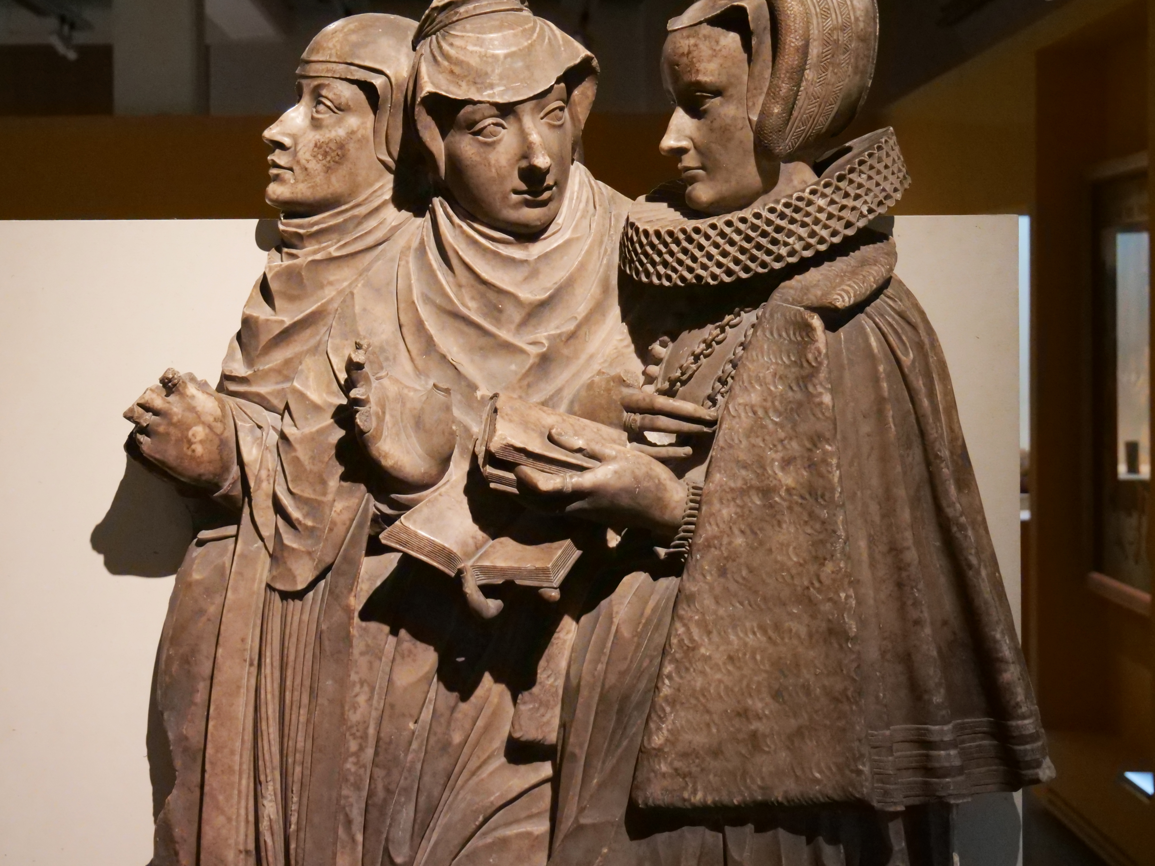 AI generated: The image shows a detailed sculpture of three people in medieval clothing. They are standing close together, with one of the figures holding a book, indicating a religious or cultural scene.