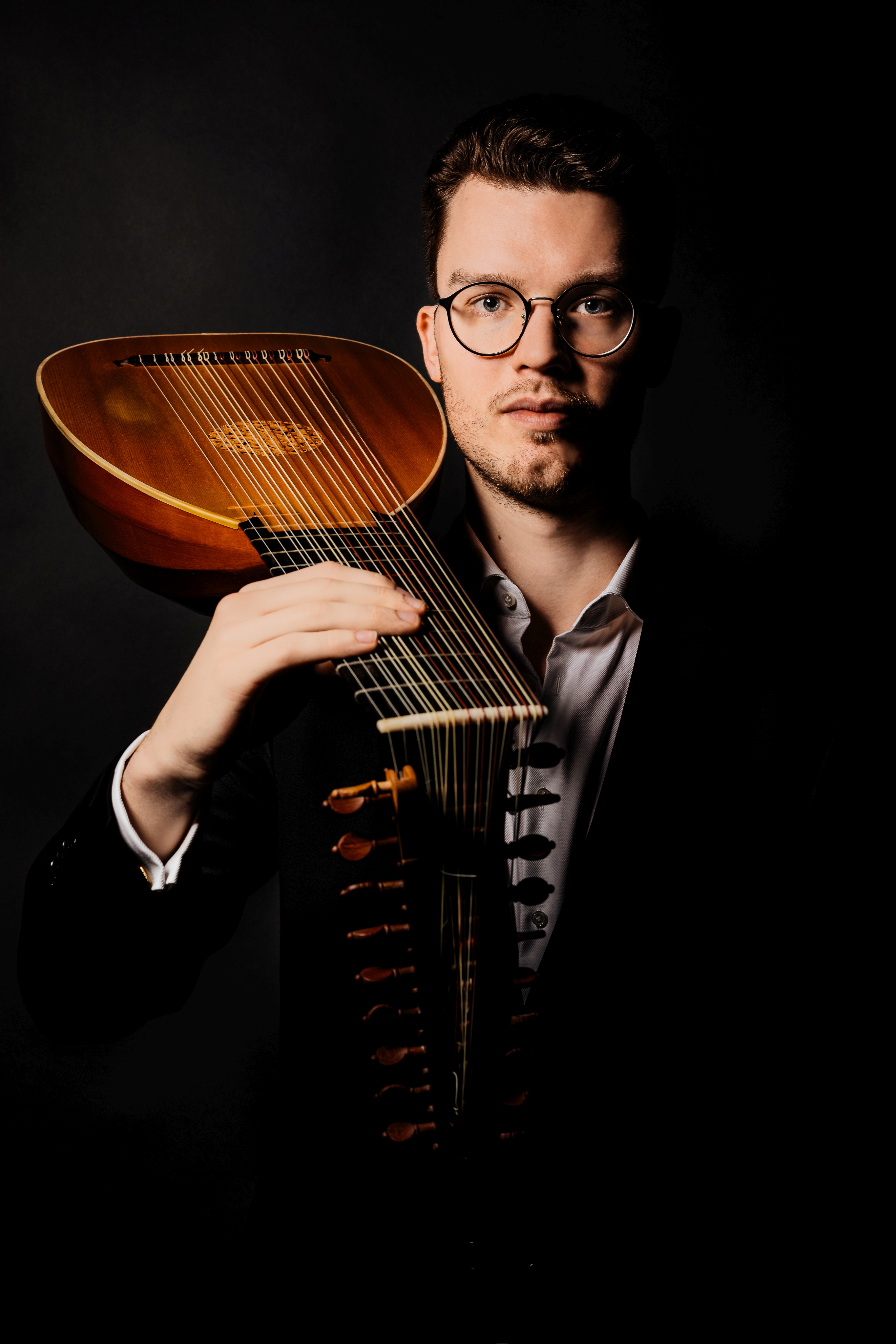 KI generiert: Ein Mann mit Brille hält eine Laute, ein historisches Saiteninstrument, vor einem dunklen Hintergrund. Der Fokus liegt auf der kunstvollen Darstellung des Instruments und der ernsten Miene des Mannes.
