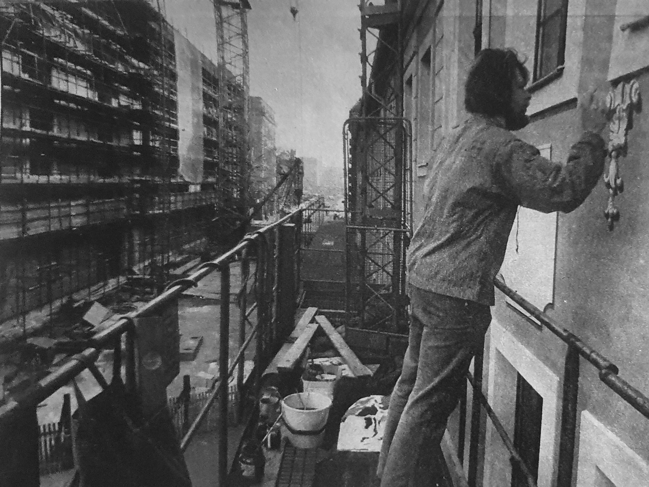 KI generiert: Ein Arbeiter restauriert oder malt die Fassade eines Gebäudes auf einem Baugerüst. Im Hintergrund sind weitere Gebäude mit Gerüsten zu sehen, was auf eine größere Baustelle oder Renovierung hinweist.