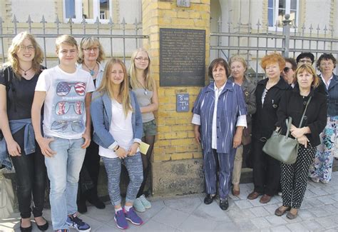 KI generiert: Eine Gruppe von Menschen steht vor einer Mauer mit einer Gedenktafel, möglicherweise bei einer Gedenkveranstaltung oder Besichtigung. Die Gruppe besteht aus verschiedenen Altersgruppen, was auf ein gemeinsames Interesse oder eine Gemeinschaftsaktivität hinweist.