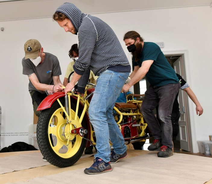 KI generiert: Das Bild zeigt eine Gruppe von Personen, die gemeinsam an einem großen, farbenfrohen Modell eines Fahrzeugs arbeiten. Der Schwerpunkt liegt auf der Teamarbeit, die erforderlich ist, um das Fahrzeug zu bewegen oder anzupassen.
