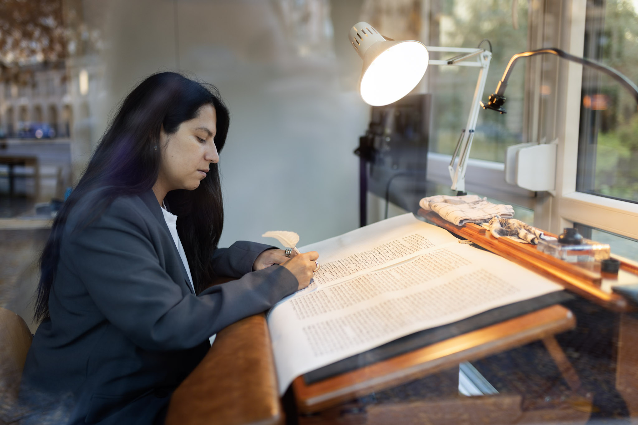 AI generated: The image shows a person working over a large document at a desk, illuminated by a lamp. She is concentrating on writing or editing the document.